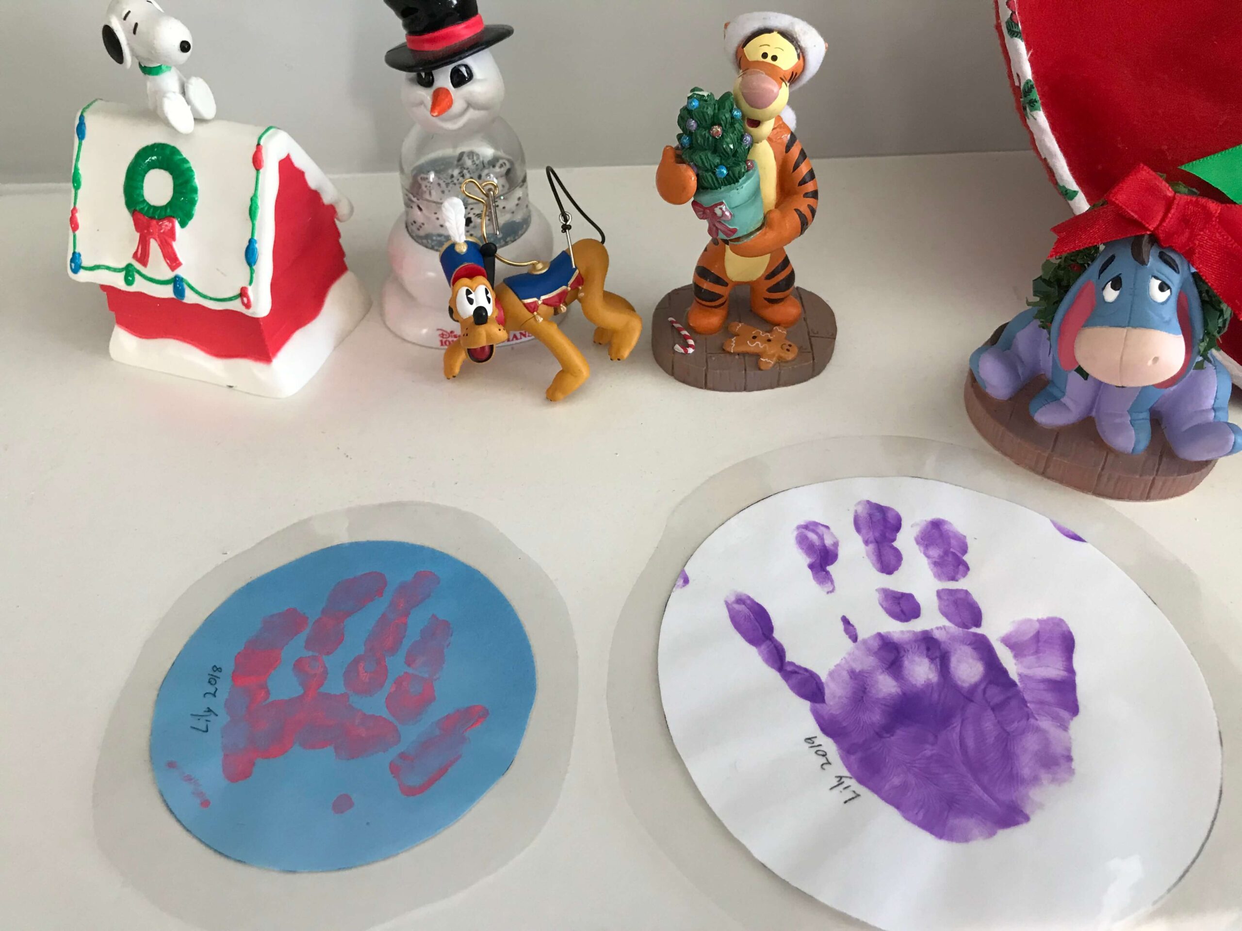 two laminated circles with handprints on them with christmas decor in the background