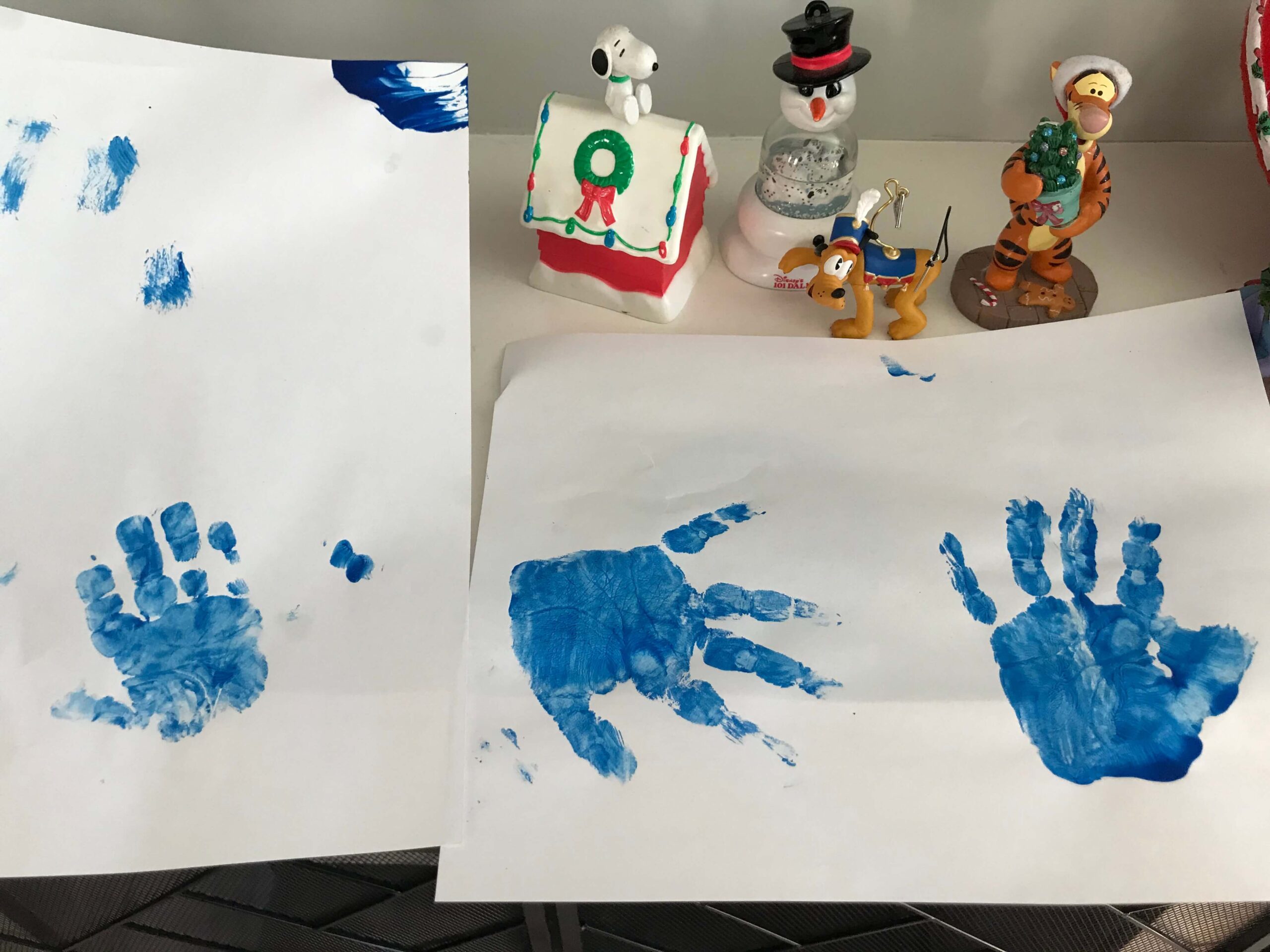 three blue painted handprints on white paper with christmas decor in background