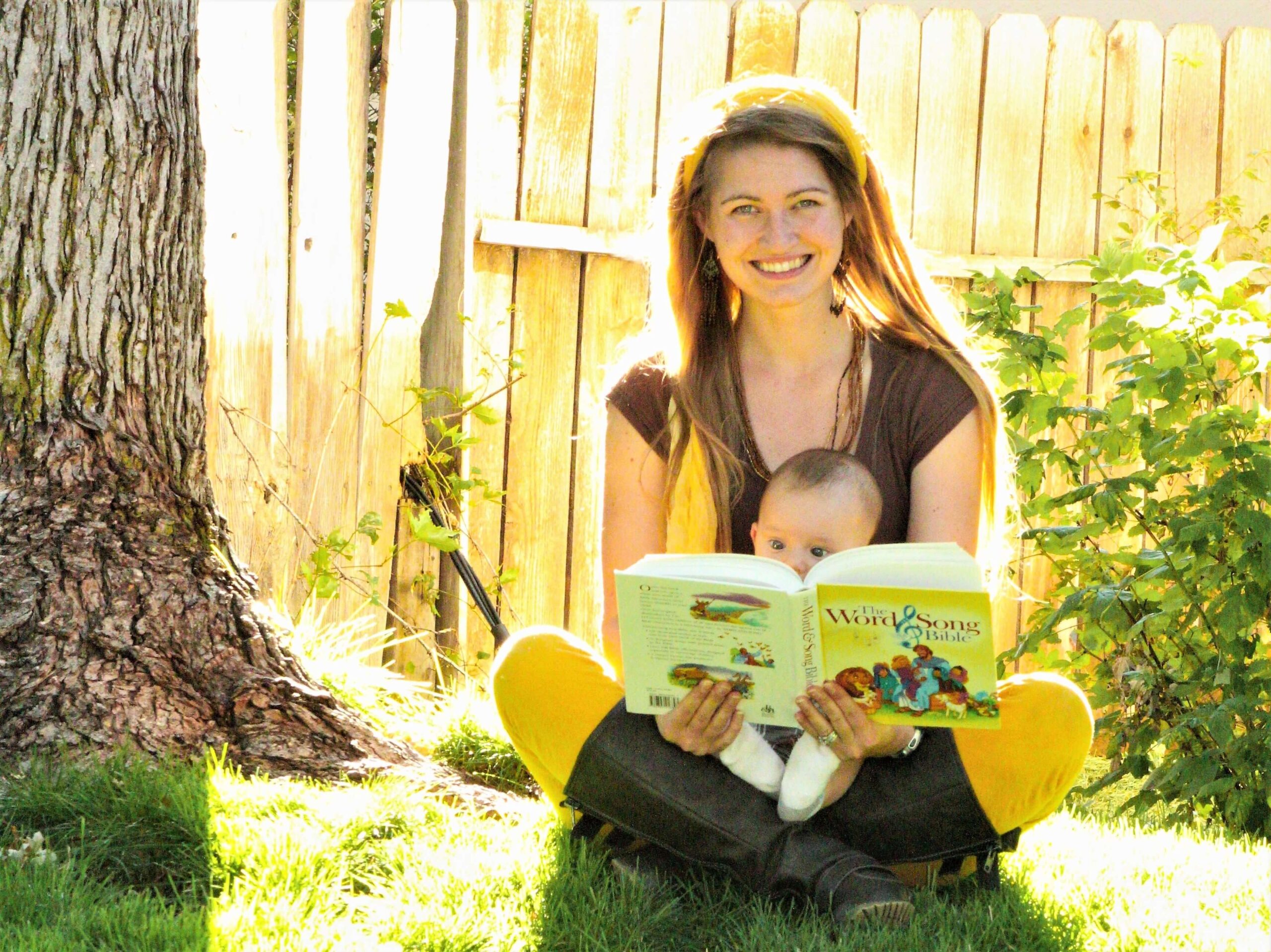 mom with baby on her lap sitting outside reading a book