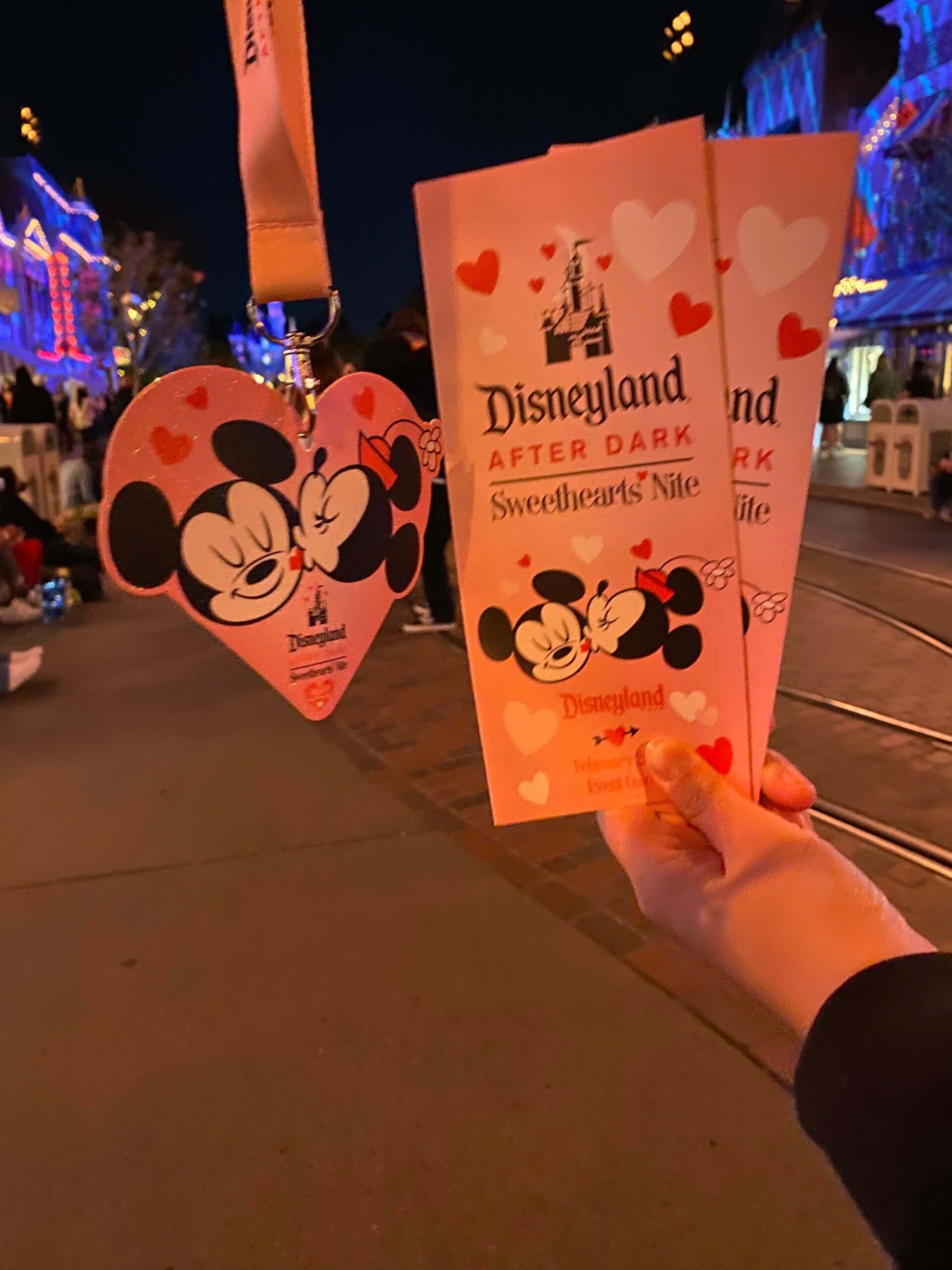 sweethearts nite lanyard and map held out with main st in backyard at disneyland
