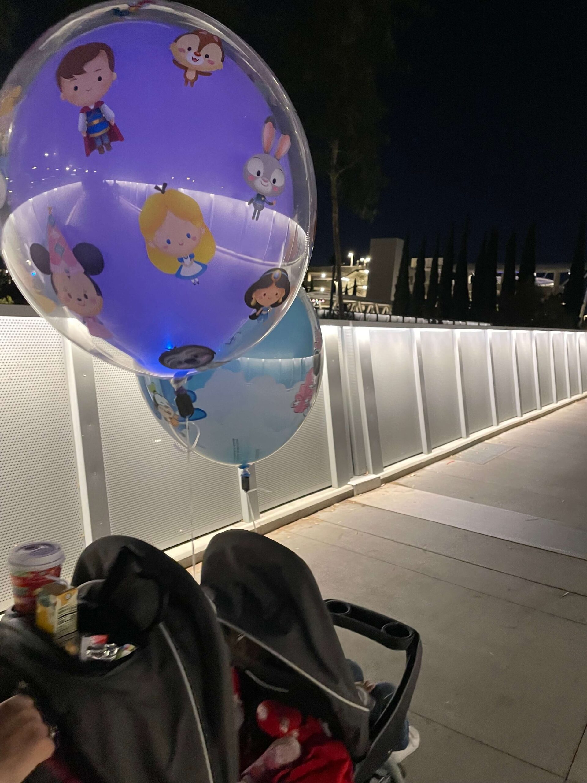 a blue disneyland balloon and a purple balloon at night attached to a stroller